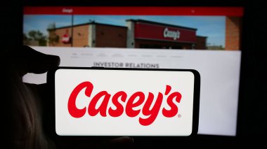 Stuttgart, Almanya - 10-18-2024: ABD 'li şirket Casey' s General Stores Inc. 'in logosuyla cep telefonu sahibi kişi iş sayfasının önünde ekranda. Telefon ekranına odaklan.