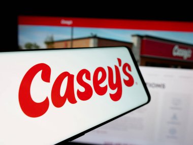 Stuttgart, Germany - 10-18-2024: Mobile phone with logo of US company Casey's General Stores Inc. on screen in front of business website. Focus on center-left of phone display. clipart