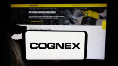 Stuttgart, Almanya - 10-18-2024: Web sayfası önünde ekranda ABD 'li makine vizyon şirketi Cognex Corporation' ın logosuyla cep telefonu tutan kişi. Telefon ekranına odaklan.
