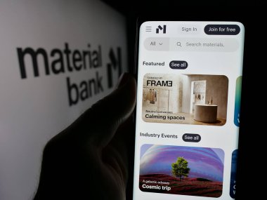 Stuttgart, Almanya - 10-18-2024: Üzerinde ABD örnek malzeme şirketi Material Bank 'ın logosu olan cep telefonu sahibi kişi iş sayfasının önünde ekranda. Telefon ekranına odaklan.