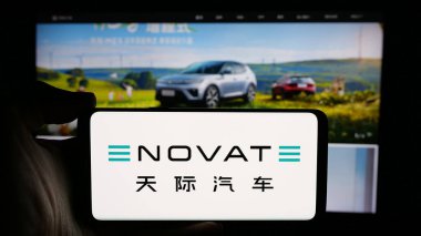 Stuttgart, Almanya - 10-18-2024: Çinli elektrikli araba şirketi Enovate Motors 'un logosuyla cep telefonu sahibi kişi iş sayfasının önünde ekranda. Telefon ekranına odaklan.