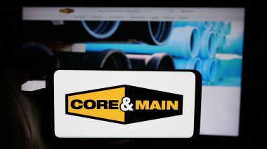 Stuttgart, Almanya - 10-18-2024: ABD 'li dağıtım şirketi Core Main Inc.' in logosuyla cep telefonu sahibi kişi iş sayfasının önünde ekranda. Telefon ekranına odaklan.