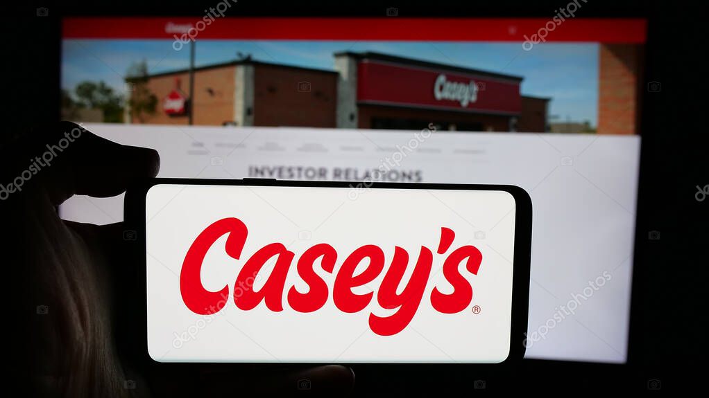 Stuttgart, Germany - 10-18-2024: Person holding cellphone with logo of US company Casey's General Stores Inc. on screen in front of business webpage. Focus on phone display.
