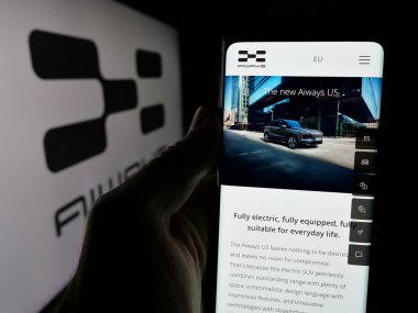 Stuttgart, Germany - 10-22-2024: Person holding smartphone with webpage of Chinese company Aiways Automobile Co. Ltd. on screen in front of logo. Focus on center of phone display. clipart