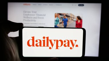 Stuttgart, Almanya - 10-22-2024: ABD 'li finans şirketi DailyPay Inc.' in logosuyla cep telefonu sahibi kişi iş sayfasının önünde ekranda. Telefon ekranına odaklan.