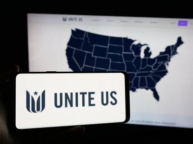Stuttgart, Almanya - 10-23-2024: Sosyal hizmet şirketi United USA Inc. 'in logosuna sahip akıllı telefon sahibi kişi web sitesi önünde ekranda. (ABD' yi Birleştir) Telefon ekranına odaklan.