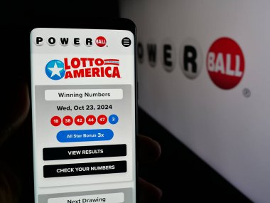 Stuttgart, Germany - 10-24-2024: Person holding cellphone with web page of US lottery game Powerball on screen in front of logo. Focus on center of phone display. clipart