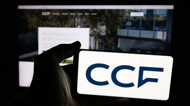 Stuttgart, Germany - 10-24-2024: Person holding smartphone with logo of company Credit Commercial de France (CCF) on screen in front of website. Focus on phone display. clipart