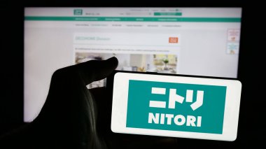 Stuttgart, Almanya - 10-28-2024: Japon perakende şirketi Nitori Co. Ltd. 'nin logosuyla cep telefonu sahibi kişi iş sayfasının önünde ekranda. Telefon ekranına odaklan.