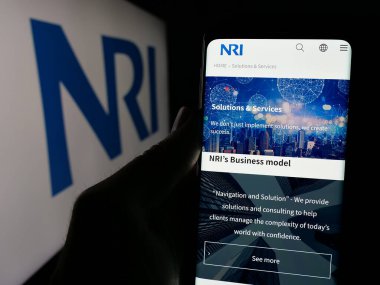 Stuttgart, Almanya - 10-28-2024: Nomura Research Institute Ltd. (NRI) adlı şirketin internet sayfası ile cep telefonu tutan kişi logolu ekranda. Telefon ekranının merkezine odaklan.