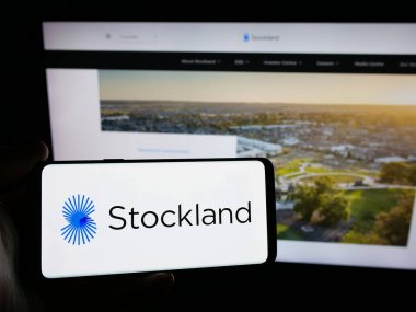 Stuttgart, Almanya - 10-30-2024: Avustralyalı Stockland Corporation Limited şirketinin logosunu elinde tutan kişi web sitesinin önünde ekranda. Telefon ekranına odaklan.