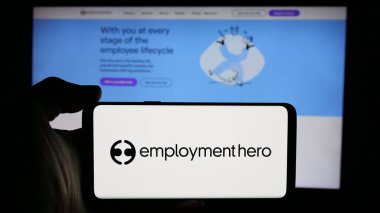 Stuttgart, Almanya - 10-31-2024: Avustralyalı şirket Employment Hero Pty 'nin logosuyla cep telefonu tutan kişi. Ltd. İş sitesinin önünde ekranda. Telefon ekranına odaklan.