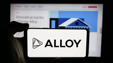 Stuttgart, Almanya - 10-31-2024: İnternet sayfası önünde üzerinde kimlik risk şirketi First Mile Group Inc. (Alloy) logosu bulunan cep telefonu bulunan kişi. Telefon ekranına odaklan.