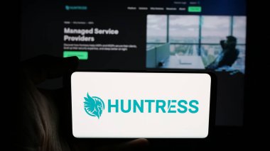 Stuttgart, Almanya - 11-06-2024: Üzerinde ABD 'li siber güvenlik şirketi Huntress Labs Inc.' in logosu olan cep telefonu sahibi kişi iş sayfasının önünde ekranda. Telefon ekranına odaklan.