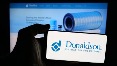 Stuttgart, Germany - 11-06-2024: Person holding mobile phone with logo of American filtration company Donaldson Company Inc. on screen in front of web page. Focus on phone display. clipart