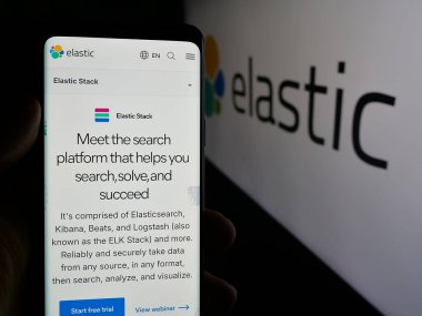 Stuttgart, Germany - 11-07-2024: Person holding cellphone with webpage of AI software company Elastic NV on screen in front of business logo. Focus on center of phone display.  clipart