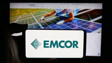 Stuttgart, Almanya - 11-07-2024: ABD 'li mühendislik şirketi EMCOR Group Inc.' nin logosuyla cep telefonu sahibi kişi iş sayfasının önünde ekranda. Telefon ekranına odaklan. 