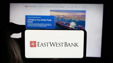 Stuttgart, Almanya - 11-07-2024: Amerikan finans hizmetleri şirketi East West Bank 'in logosunun bulunduğu cep telefonu web sayfası önünde ekranda. Telefon ekranına odaklan. 