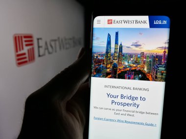 Stuttgart, Almanya - 11-07-2024: ABD 'li finans hizmetleri şirketi East West Bank' in web sayfası ile cep telefonu logosu önünde ekranda. Telefon ekranının merkezine odaklan. 