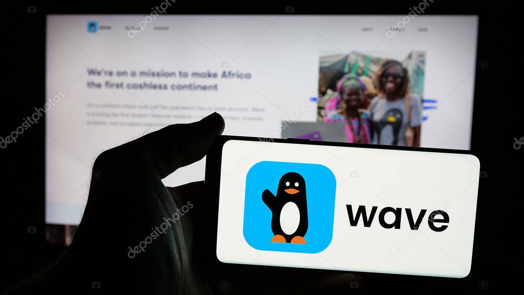 Stuttgart, Germany - 10-31-2024: Person holding smartphone with logo of Sengalese company Wave Mobile Money Inc. on screen in front of website. Focus on phone display.