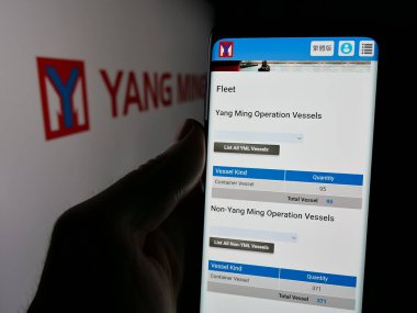 Stuttgart, Germany - 11-07-2024: Person holding cellphone with webpage of company Yang Ming Marine Transport Corporation on screen in front of logo. Focus on center of phone display. clipart