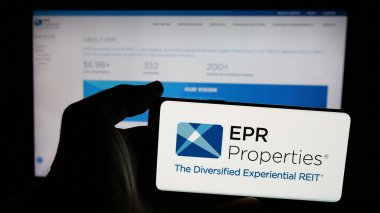 Stuttgart, Germany - 11-07-2024: Person holding mobile phone with logo of US real estate company EPR Properties on screen in front of business web page. Focus on phone display. clipart