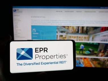 Stuttgart, Germany - 11-07-2024: Person holding smartphone with logo of US real estate company EPR Properties on screen in front of website. Focus on phone display. clipart