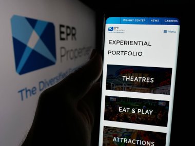 Stuttgart, Germany - 11-07-2024: Person holding cellphone with webpage of US real estate company EPR Properties on screen in front of logo. Focus on center of phone display. clipart