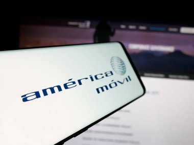 Stuttgart, Almanya - 11-08-2024: Meksikalı Amerikan Movil S.A.B. şirketinin logosuna sahip akıllı telefon De C.V. iş sitesinin önünde ekranda. Telefon ekranının soluna odaklan.