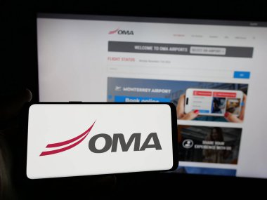 Stuttgart, Almanya - 11-11-2024: Web sitesinin önünde Grupo Aeroportuario del Centro Norte (OMA) şirketinin logosuna sahip akıllı telefon sahibi kişi. Telefon ekranına odaklan.