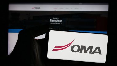 Stuttgart, Almanya - 11-11-2024: Web sayfası önünde Grupo Aeroportuario del Centro Norte (OMA) şirketinin logosuna sahip cep telefonu sahibi kişi. Telefon ekranına odaklan.