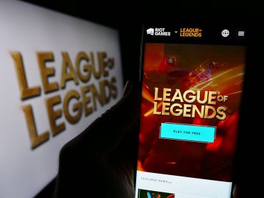 Stuttgart, Germany - 12-27-2023: Person holding cellphone with webpage of online multiplayer video game League of Legends (LoL) in front of logo. Focus on center of phone display. clipart