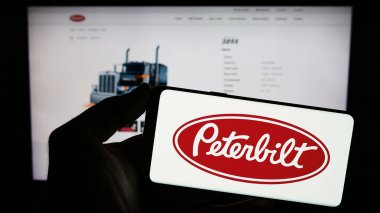 Stuttgart, Almanya - 12-27-2023: İnternet sayfası önünde üzerinde ABD 'li kamyonet üreticisi Peterbilt Motor Şirketi' nin logosu olan cep telefonu tutan kişi. Telefon ekranına odaklan.