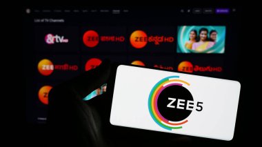 Stuttgart, Germany - 12-27-2023: Person holding smartphone with logo of Indian video streaming platform company ZEE5 in front of website. Focus on phone display. clipart