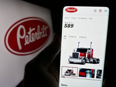 Stuttgart, Almanya - 12-27-2023: ABD 'li kamyonet işçisi Peterbilt Motors Company' nin logolu web sayfası ile cep telefonu tutan kişi. Telefon ekranının merkezine odaklan.