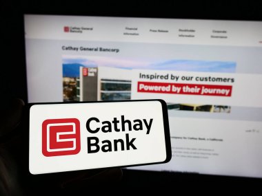 Stuttgart, Germany - 12-23-2023: Person holding smartphone with logo of US company Cathay General Bancorp (Cathay Bank) in front of website. Focus on phone display. clipart