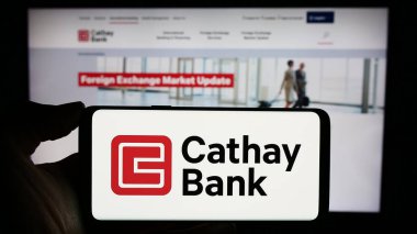 Stuttgart, Almanya - 12-23-2023: ABD 'li Cathay General Bancorp (Cathay Bank) şirketinin logosuyla cep telefonu sahibi kişi iş sayfası önünde. Telefon ekranına odaklan.