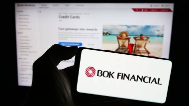 Stuttgart, Almanya - 12-23-2023: İnternet sayfası önünde ABD 'li finans şirketi BOK Financial Corporation' ın logosunun bulunduğu cep telefonu sahibi kişi. Telefon ekranına odaklan.