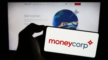 Stuttgart, Germany - 12-23-2023: Person holding cellphone with logo of British payments company TTT Moneycorp Limited in front of business webpage. Focus on phone display. clipart