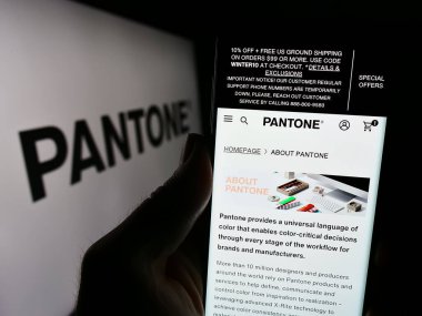 Stuttgart, Almanya - 12-28-2023: ABD 'li renkli çözümler şirketi Pantone LLLC' nin web sitesine sahip cep telefonu sahibi kişi iş logosu önünde. Telefon ekranının merkezine odaklan.