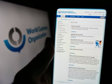 Stuttgart, Almanya - 12-28-2023: Logo önünde Dünya Gümrük Örgütü (WCO) web sayfası ile cep telefonu tutan kişi. Telefon ekranının merkezine odaklan.
