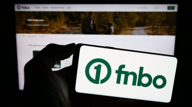 Stuttgart, Almanya - 12-28-2023: Amerikan finans şirketi First National Bank Omaha 'nın (FNBO) logosuna sahip cep telefonu sahibi kişi web sayfasının önünde. Telefon ekranına odaklan.