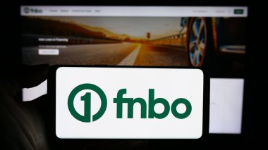 Stuttgart, Germany - 12-28-2023: Person holding cellphone with logo of US financial company First National Bank Omaha (FNBO) in front of business webpage. Focus on phone display. clipart