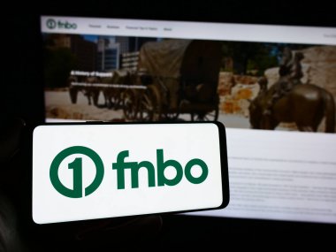 Stuttgart, Germany - 12-28-2023: Person holding smartphone with logo of US financial company First National Bank Omaha (FNBO) in front of website. Focus on phone display. clipart