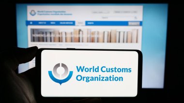 Stuttgart, Germany - 12-28-2023: Person holding cellphone with logo of World Customs Organization (WCO) in front of webpage. Focus on phone display. clipart