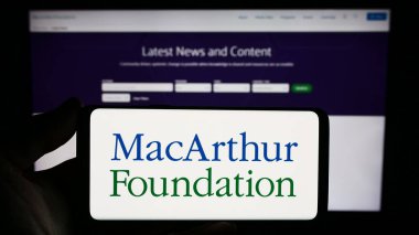Stuttgart, Almanya - 12-29-2023: John D. ve Catherine T. MacArthur Vakfı 'nın logosunun bulunduğu akıllı telefonu web sitesinin önünde tutan kişi. Telefon ekranına odaklan.