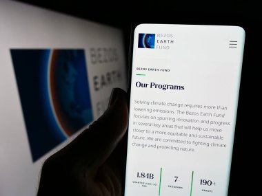 Stuttgart, Almanya - 12-29-2023: Çevre örgütü Bezos Earth Fund 'un web sayfası ile logo önünde cep telefonu tutan kişi. Telefon ekranının merkezine odaklan.