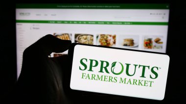 Stuttgart, Almanya - 12-31-2023: ABD 'li perakende şirketi Sprouts Farmers Market Inc.' in logosuyla cep telefonu sahibi kişi iş sayfası önünde. Telefon ekranına odaklan.