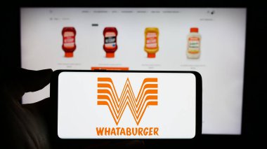 Stuttgart, Almanya - 12-31-2023: ABD 'li fast food şirketi Whataburger Restaurants LLC' nin logosuyla cep telefonu tutan kişi iş sayfasının önünde. Telefon ekranına odaklan.