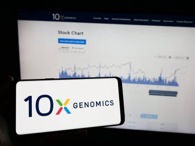 Stuttgart, Almanya - 12-31-2023: Amerikan biyoteknoloji şirketi 10x Genomics Inc. 'in logosu olan cep telefonu sahibi kişi iş sayfasının önünde. Telefon ekranına odaklan.